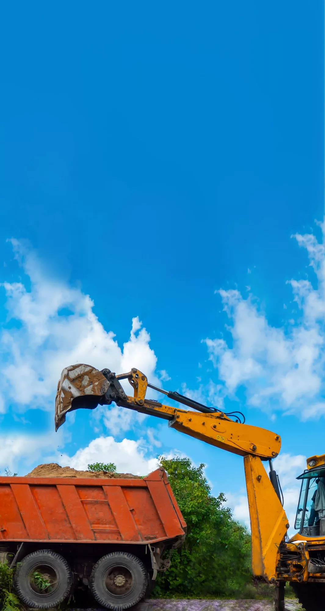 Orange excavator unloads sand from a dump truck. Dig in the agricultural area.